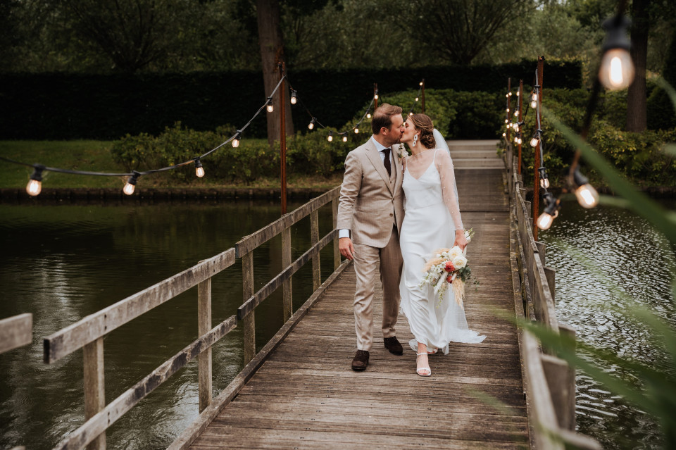 een bruid en bruidegom lopen over een houten brug boven een vijver