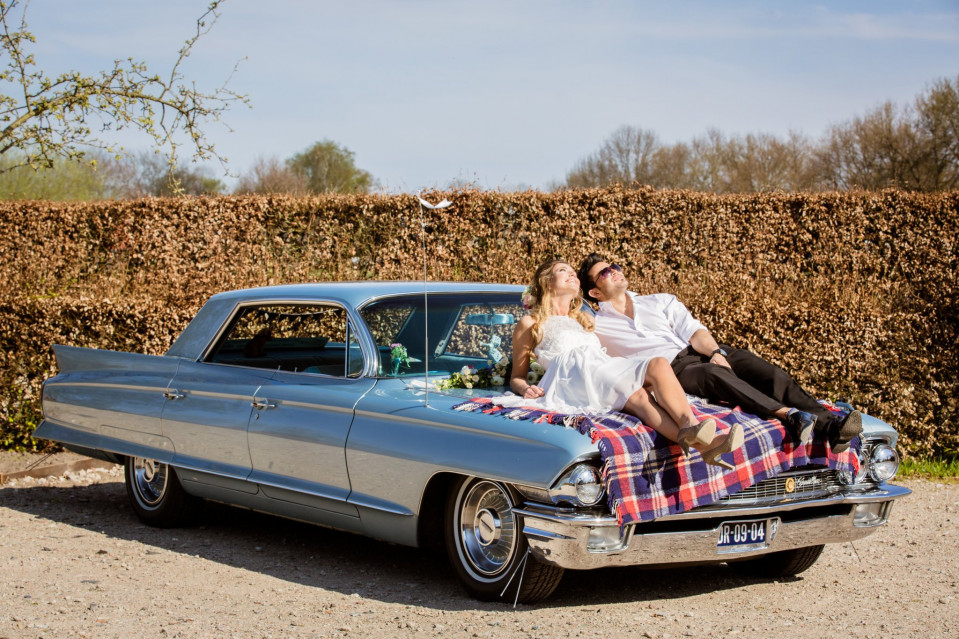 een stel dat op de motorkap van een klassieke auto zit