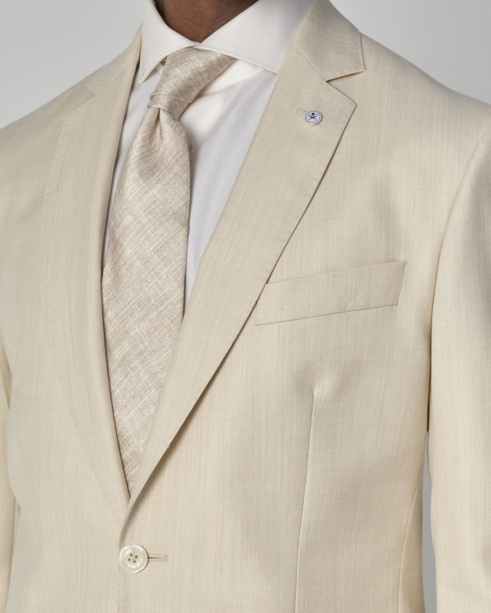 een man in een crèmekleurig pak en stropdas