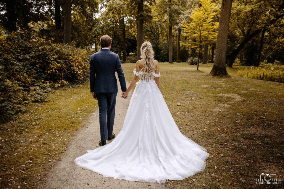 de achterkant van een bruid en bruidegom die een pad in het bos lopen