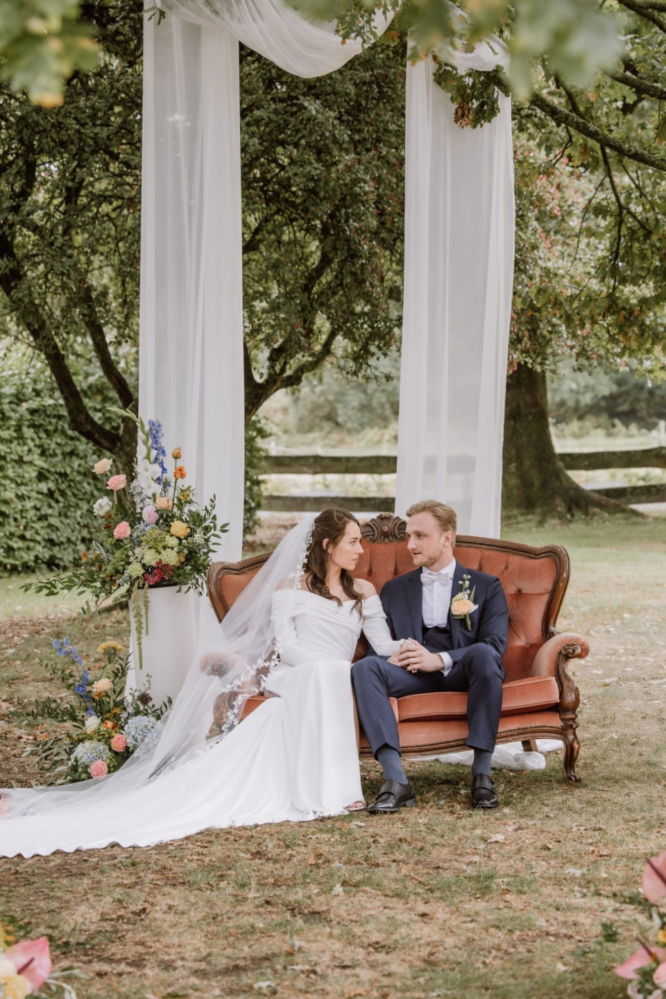 het bruidspaar dat op een bank zit onder een luifel