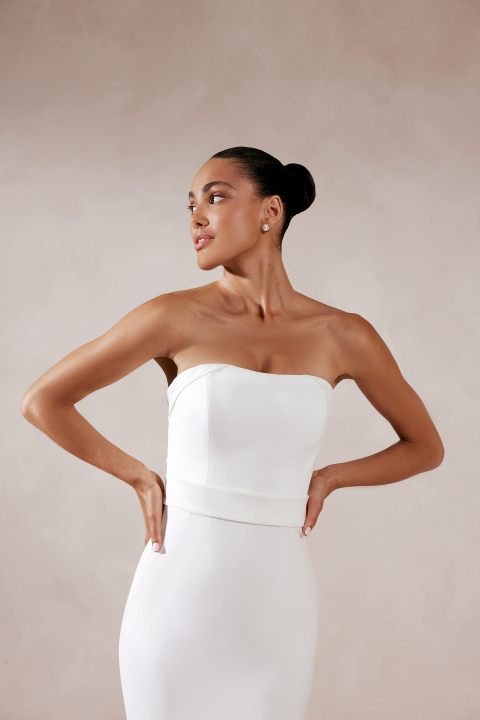 de achterkant van een vrouw in een witte strapless jurk, met haar handen op haar heupen en haar hand op haar heup