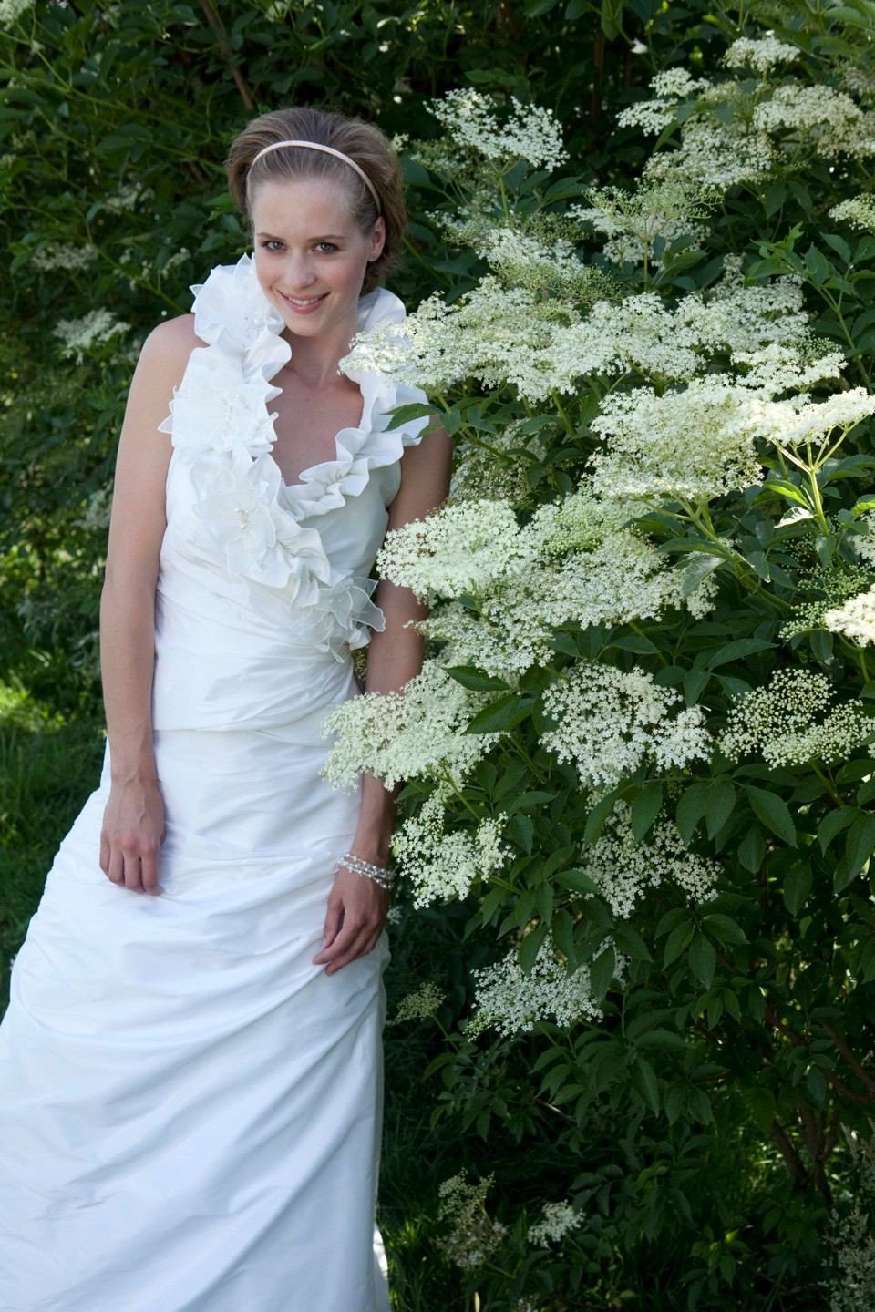een vrouw in een witte trouwjurk die naast wat witte bloemen staat