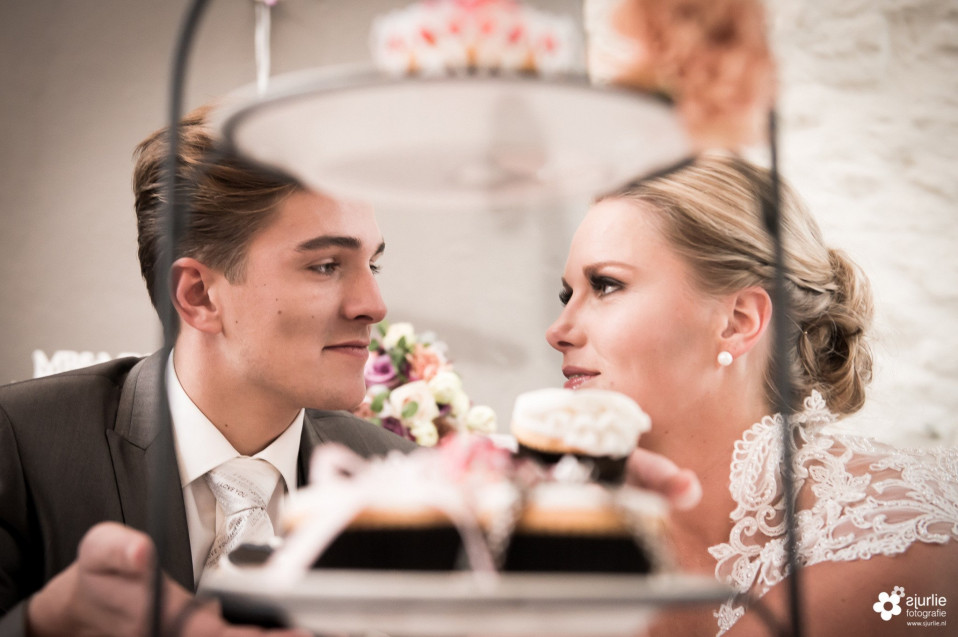 een bruid en bruidegom kijken naar elkaar terwijl ze cupcakes vasthouden