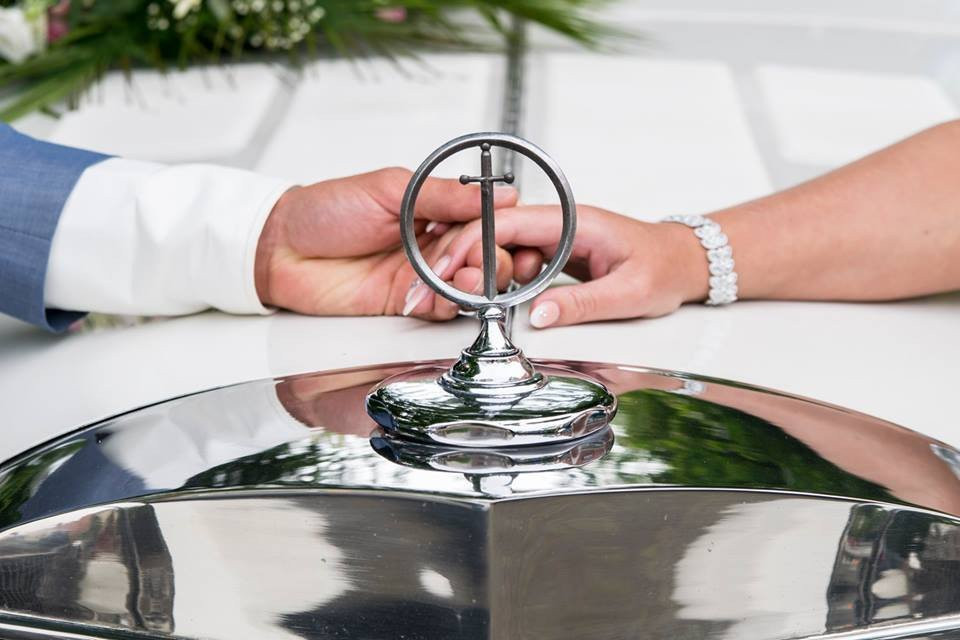 een bruid en bruidegom houden elkaars hand vast op de motorkap van een auto