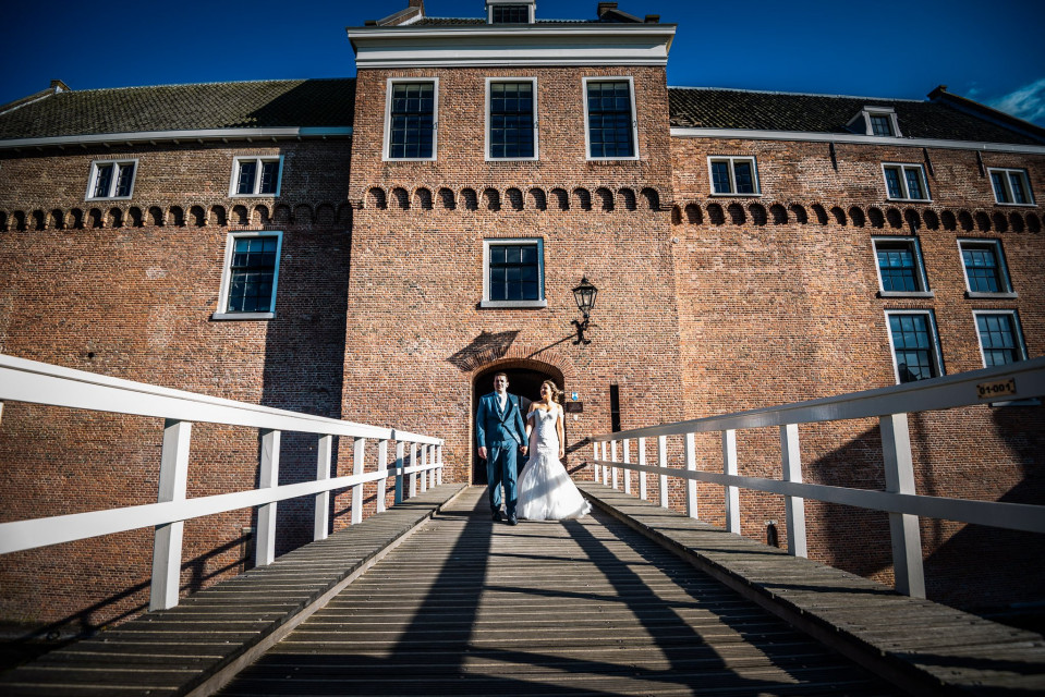 een bruid en bruidegom lopen op een brug voor een kasteel