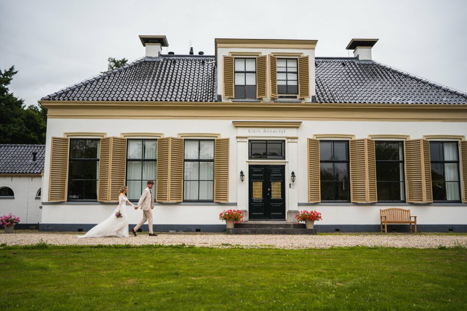 een bruid en bruidegom die voor een huis lopen