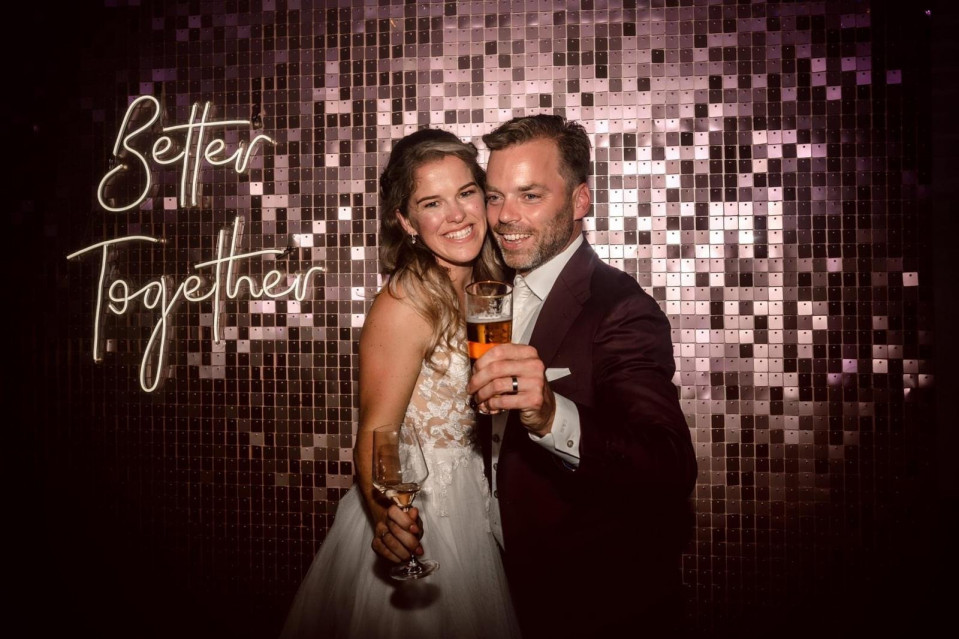 een bruidspaar poseert voor een foto met een bord waarop 'beter samen' staat
