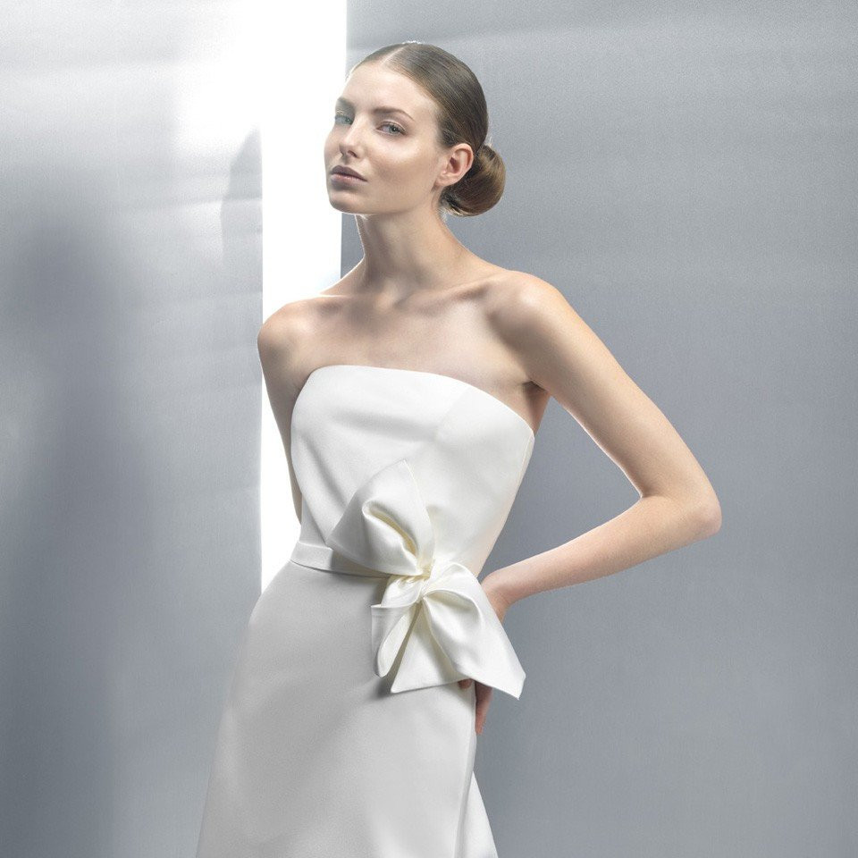 een model draagt een strapless witte jurk met een strik