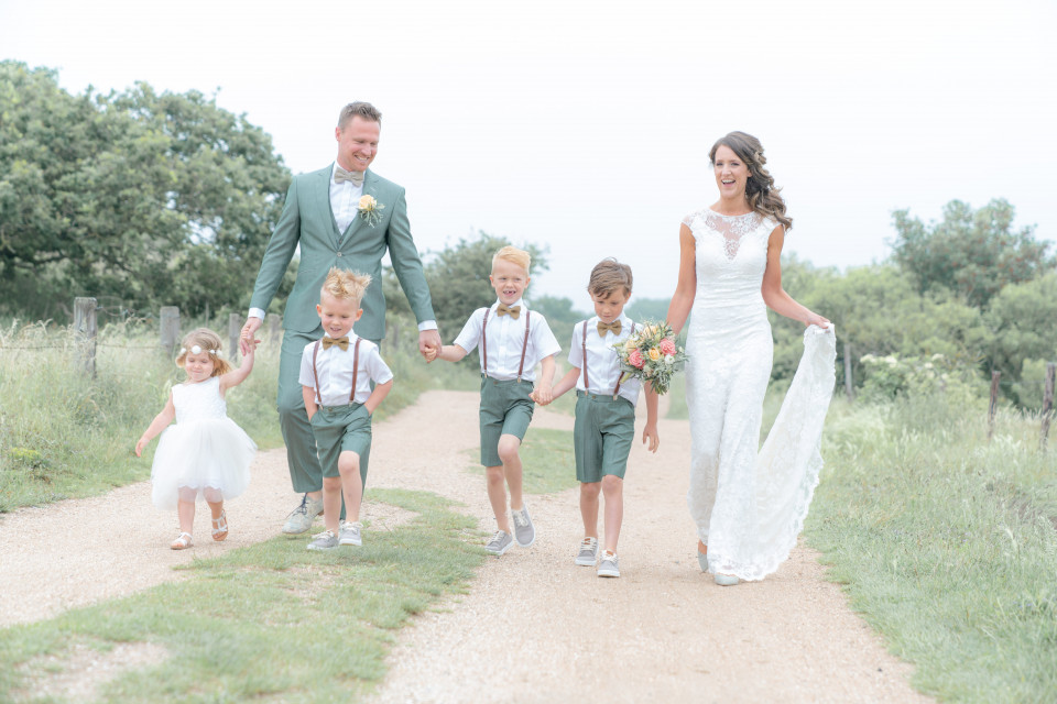 een bruid en bruidegom met hun kinderen die over een zandweg lopen