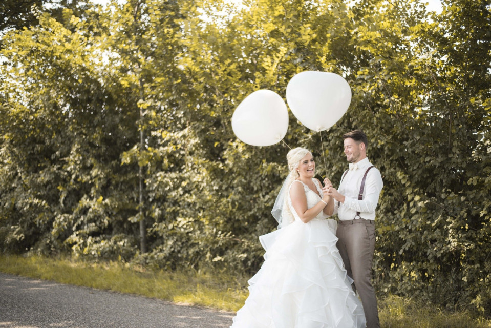 een bruid en bruidegom die ballonnen vasthouden op een landweg