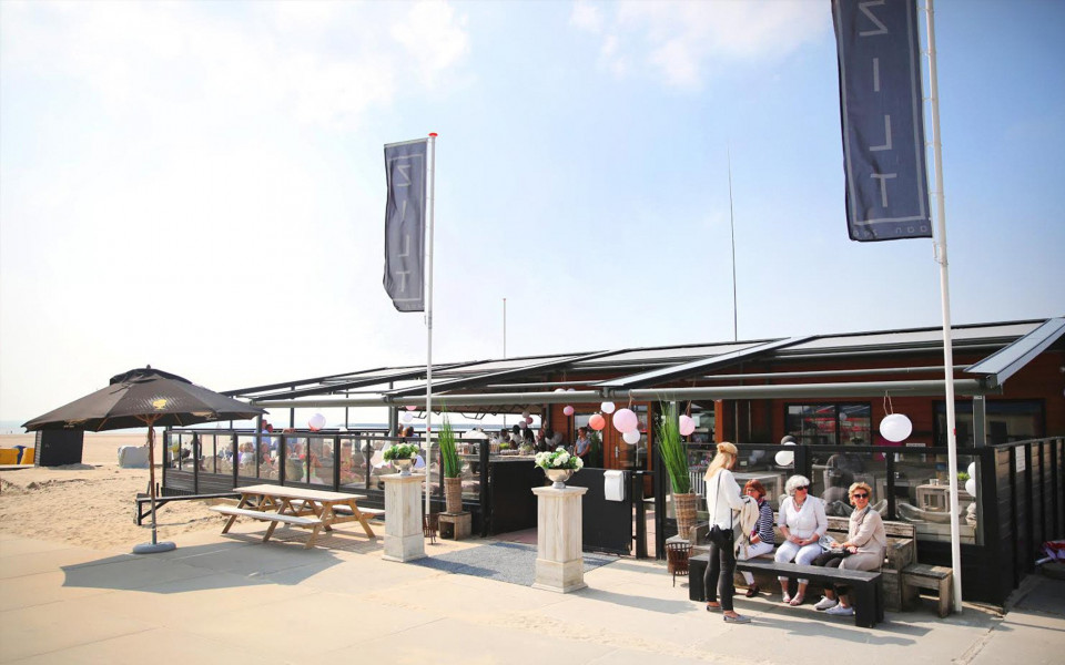 een groep mensen zit op het strand bij een restaurant