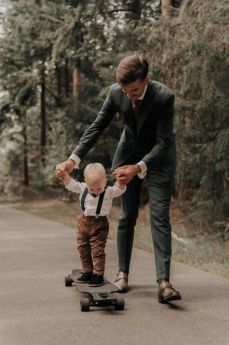 een man in pak en stropdas die een kind op een skateboard vasthoudt