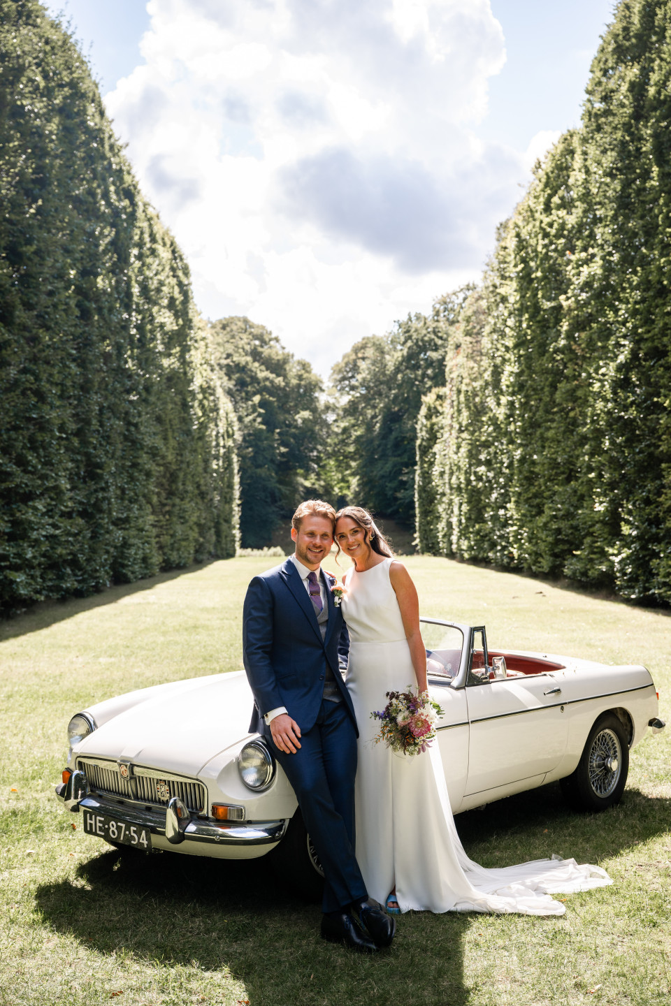 een bruid en bruidegom die poseren voor een klassieke auto