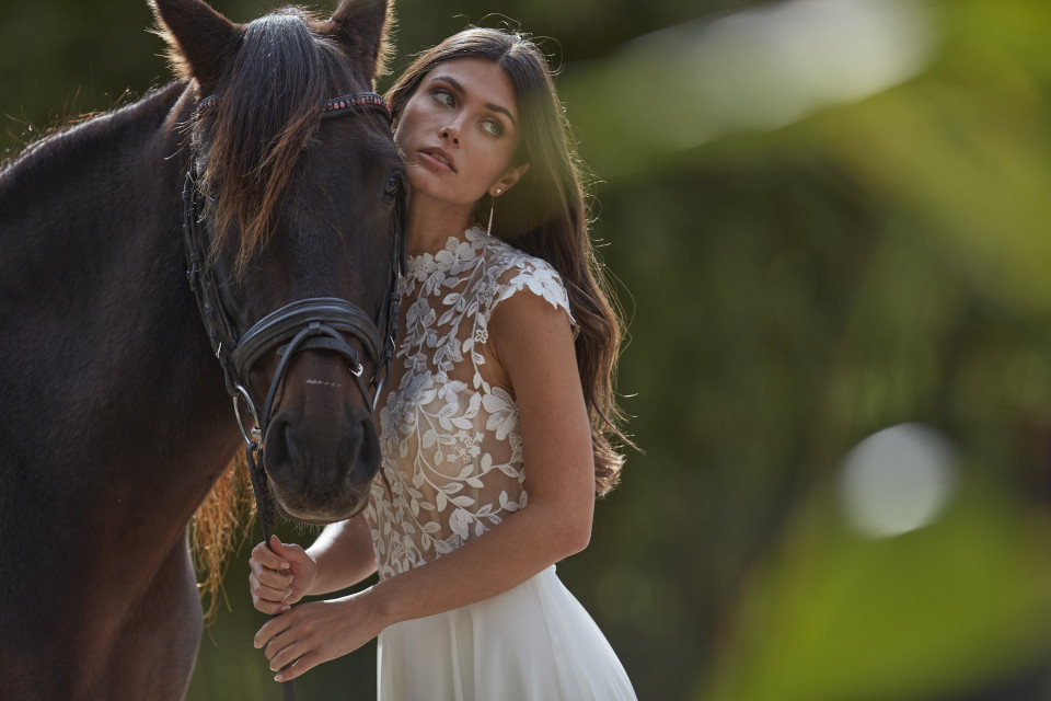 een vrouw in een trouwjurk die naast een paard staat
