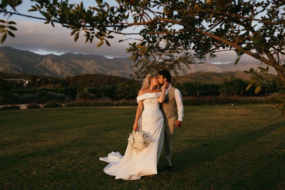 een bruid en bruidegom die kussen in een veld met bergen op de achtergrond
