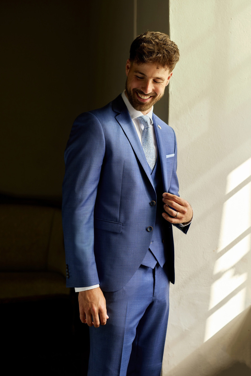 een man in een blauw pak die bij een muur staat