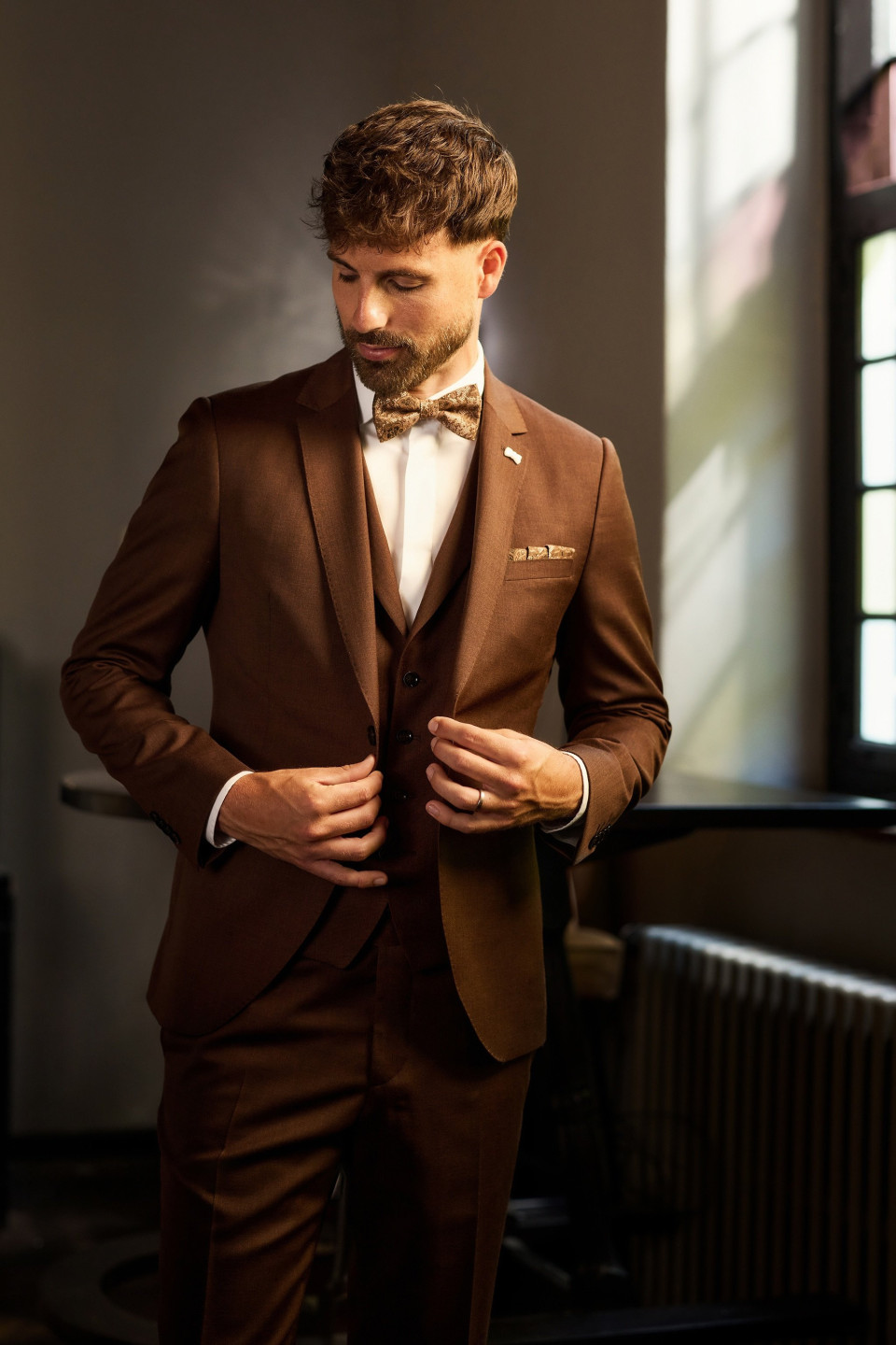 een man in een bruin pak die zijn vlinderdas aanpast