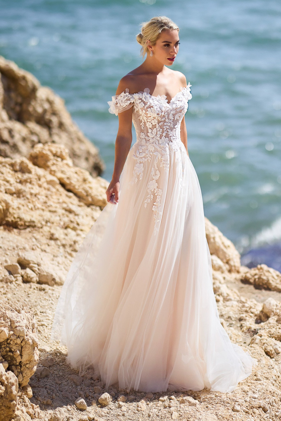 een vrouw in een trouwjurk die op een rotsachtig strand staat