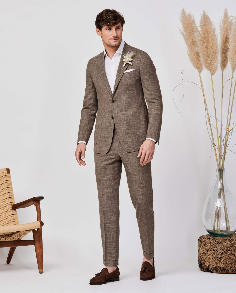 een man in een pak en stropdas die naast een stoel staat