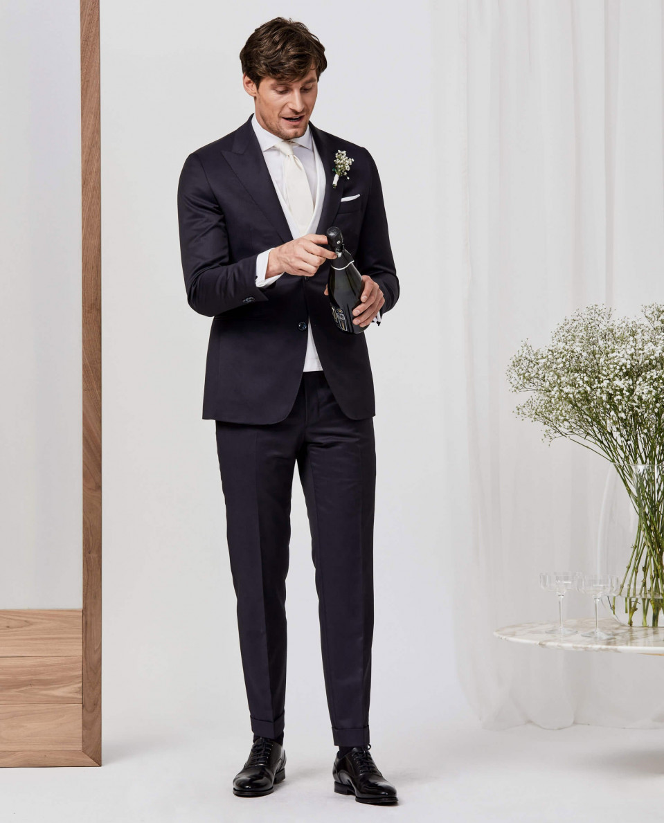 een man in een pak en stropdas die naast een vaas met bloemen staat