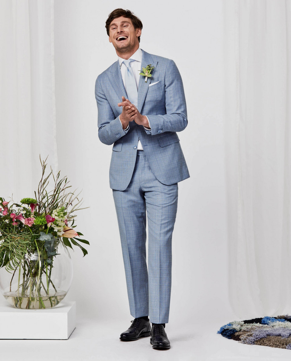 een man in een blauw pak en stropdas die naast een vaas met bloemen staat