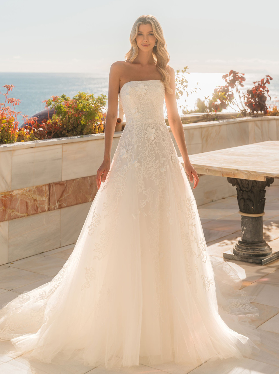 een vrouw in een trouwjurk die voor de oceaan staat