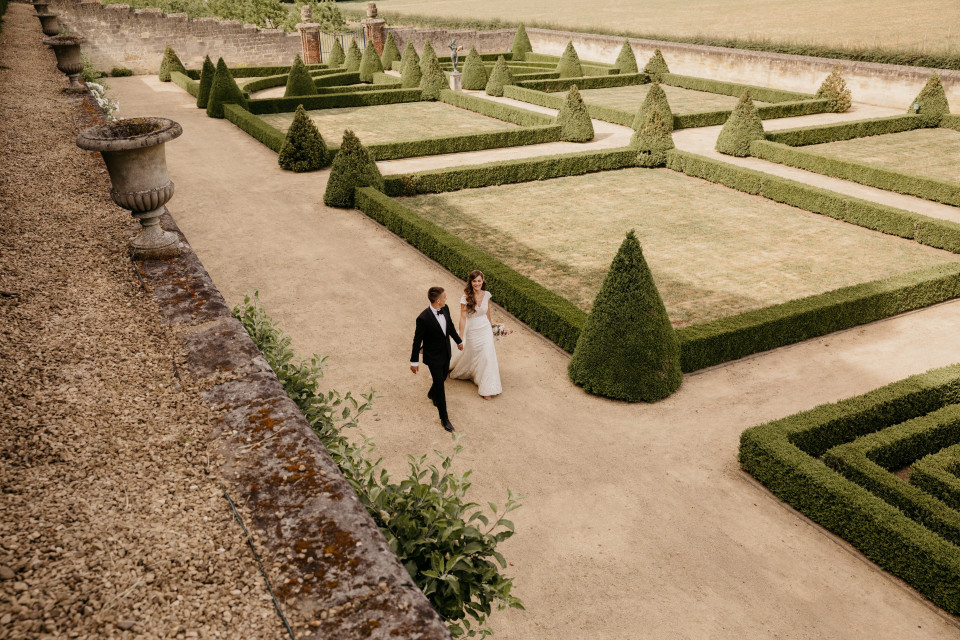 een bruid en bruidegom lopen door een formele tuin