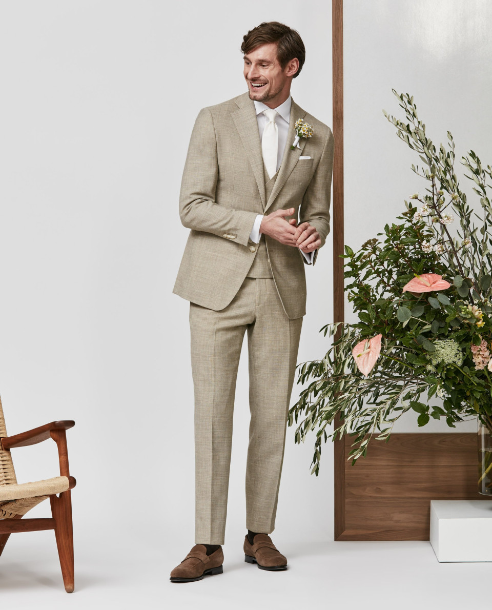 een man in een beige pak en wit overhemd