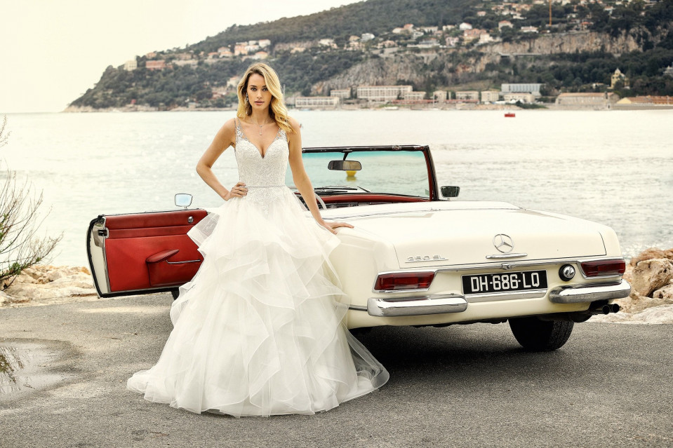 een mooie bruid in een trouwjurk staat naast een klassieke auto