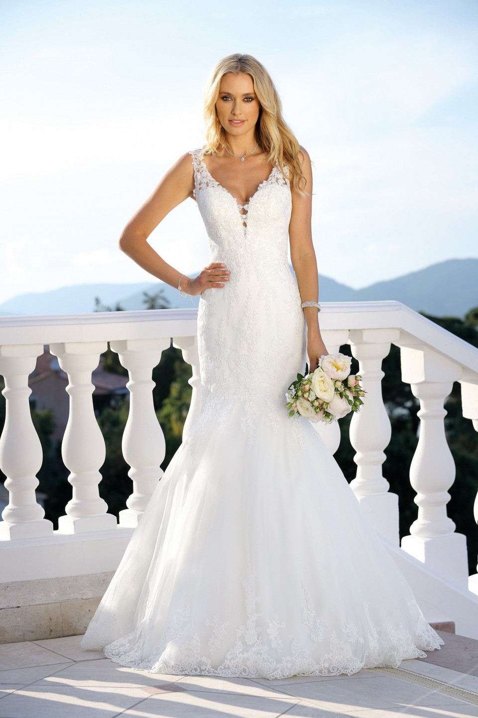 een mooie blonde vrouw in een trouwjurk staat op een balkon