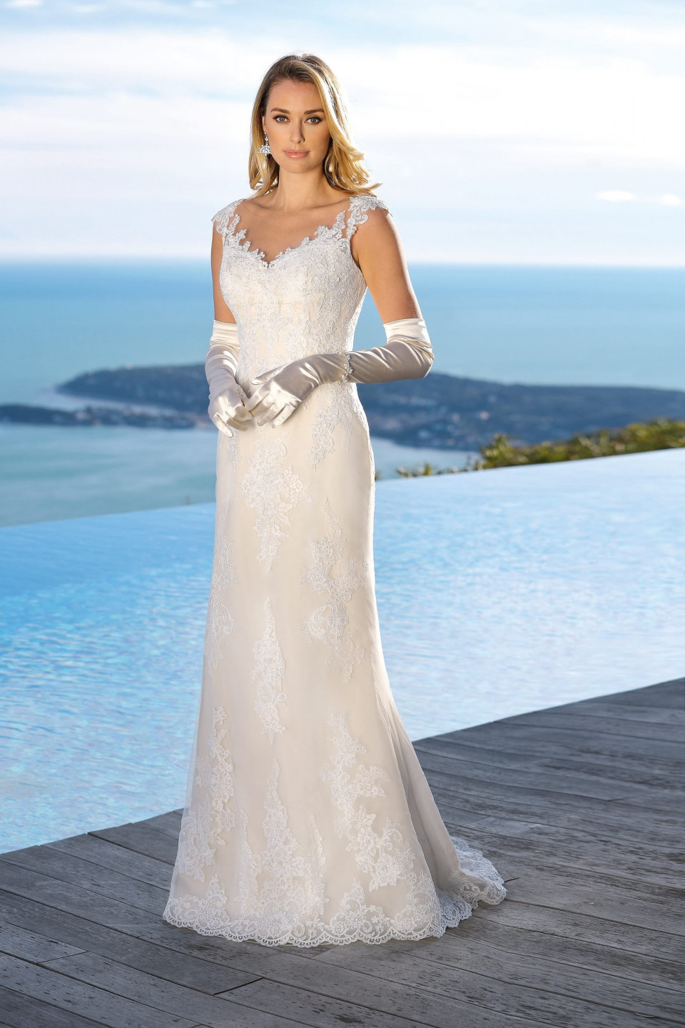 een vrouw in een trouwjurk staat op een houten dek met uitzicht op de oceaan