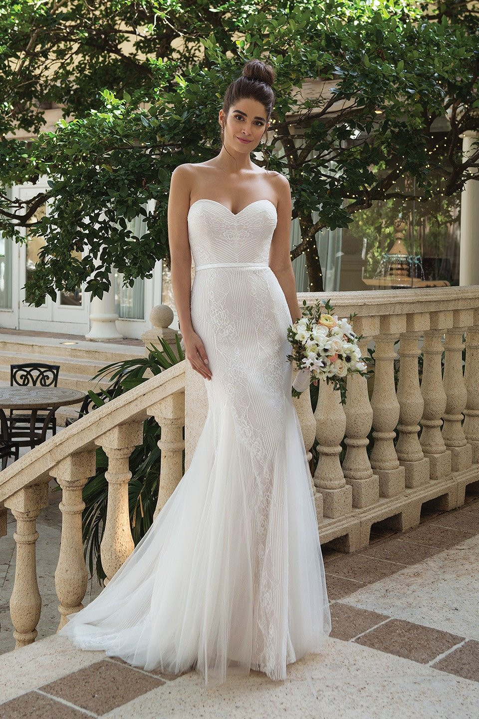 een mooie bruid in een strapless trouwjurk die op een balkon staat