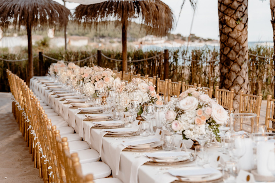 een lange tafel opgezet met witte en gouden borden en stoelen