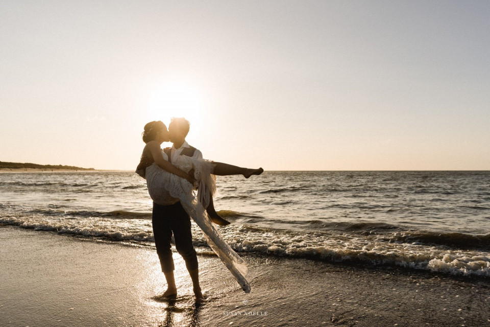 een bruid en bruidegom staan op het strand bij zonsondergang