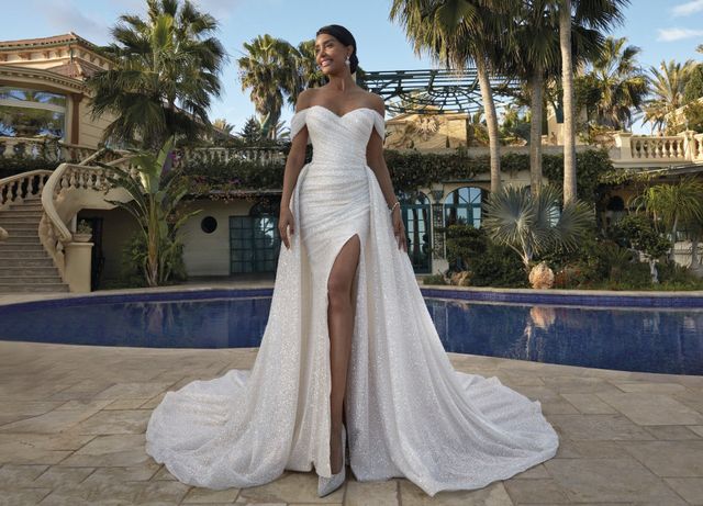 Braut in langem glitzerndem Brautkleid mit Beinschlitz steht vor einem Pool