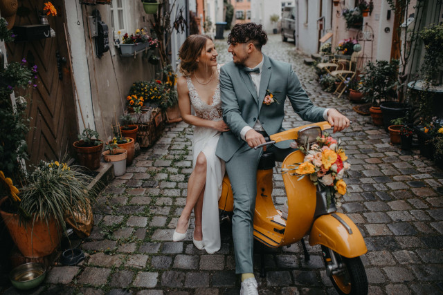 Brautpaar sitzt auf einer gelben Vespa welche mit Blumen verziert ist