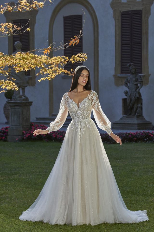 Braut in langärmligen Brautkleid steht in einem grünen Garten