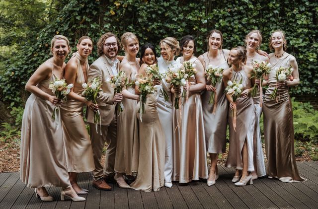 A group of bridesmaids in champagne and gold satin dresses holding bouquets.
