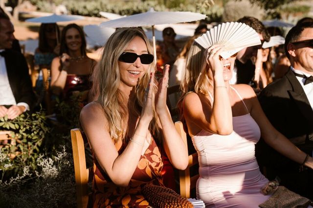 Two female guests in sunglasses applaud and watch the ceremony.