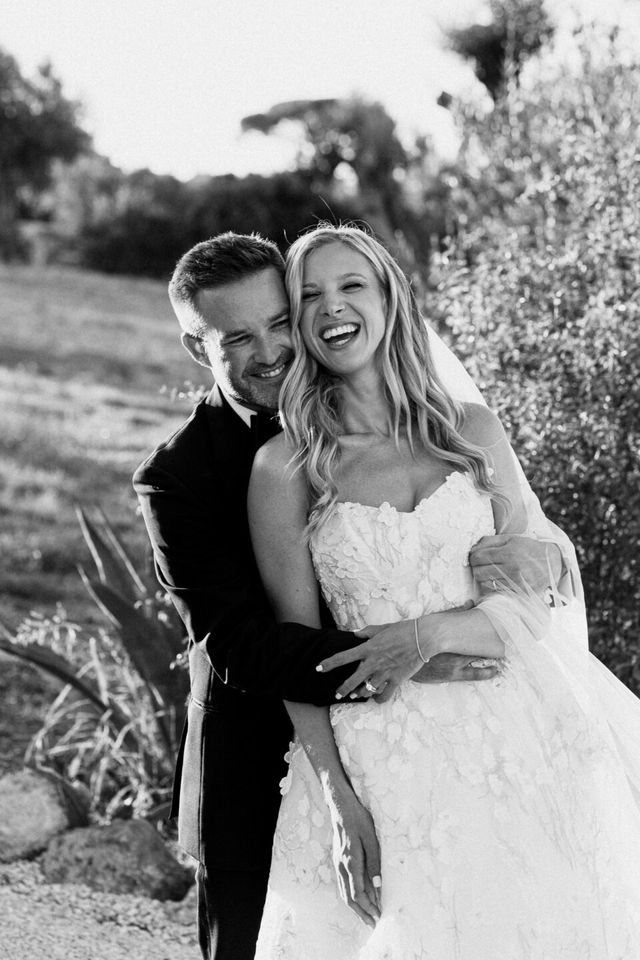 A black-and-white portrait of a laughing couple embracing in a green garden.