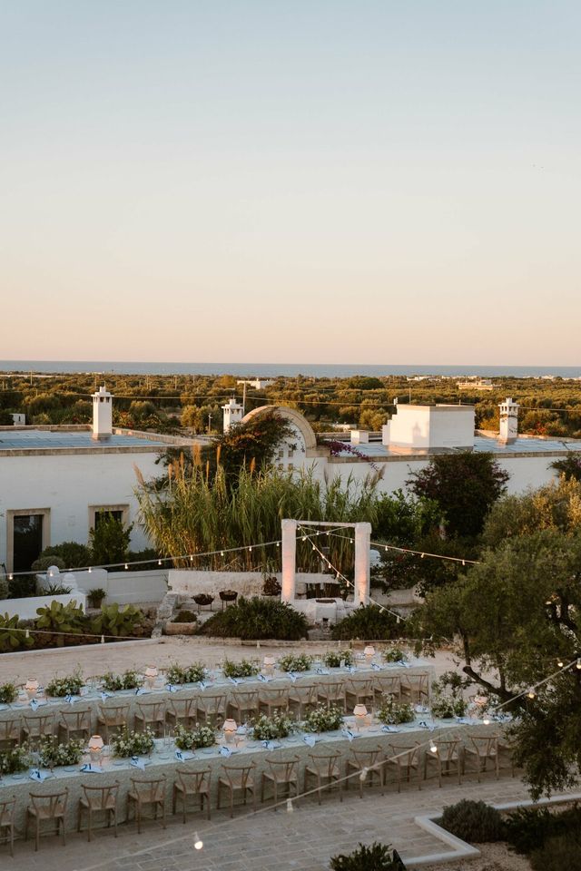 Overview of long set dinner tables on a courtyard between white buildings at a wedding.