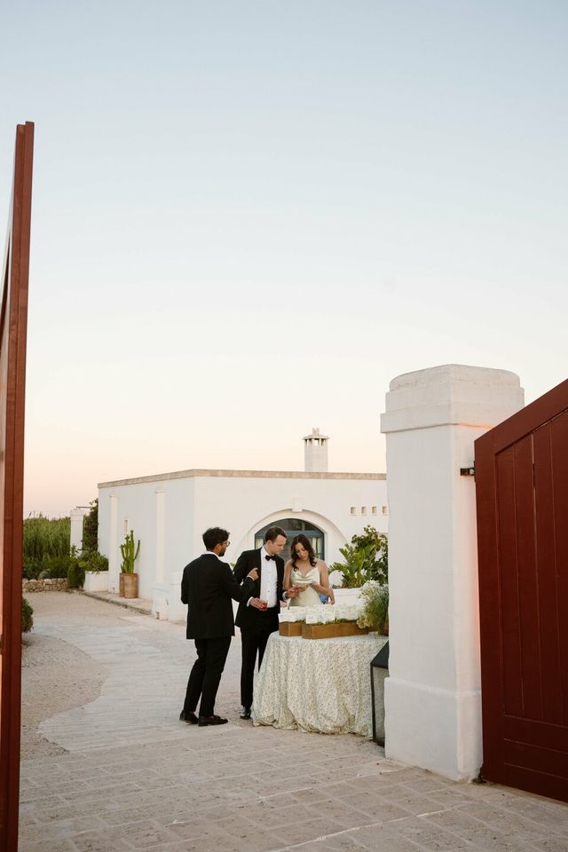 The couple stands by the cake table as a guest looks on.