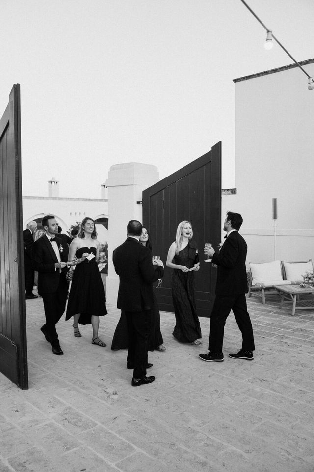 A black and white photo of elegantly dressed guests standing and chatting.