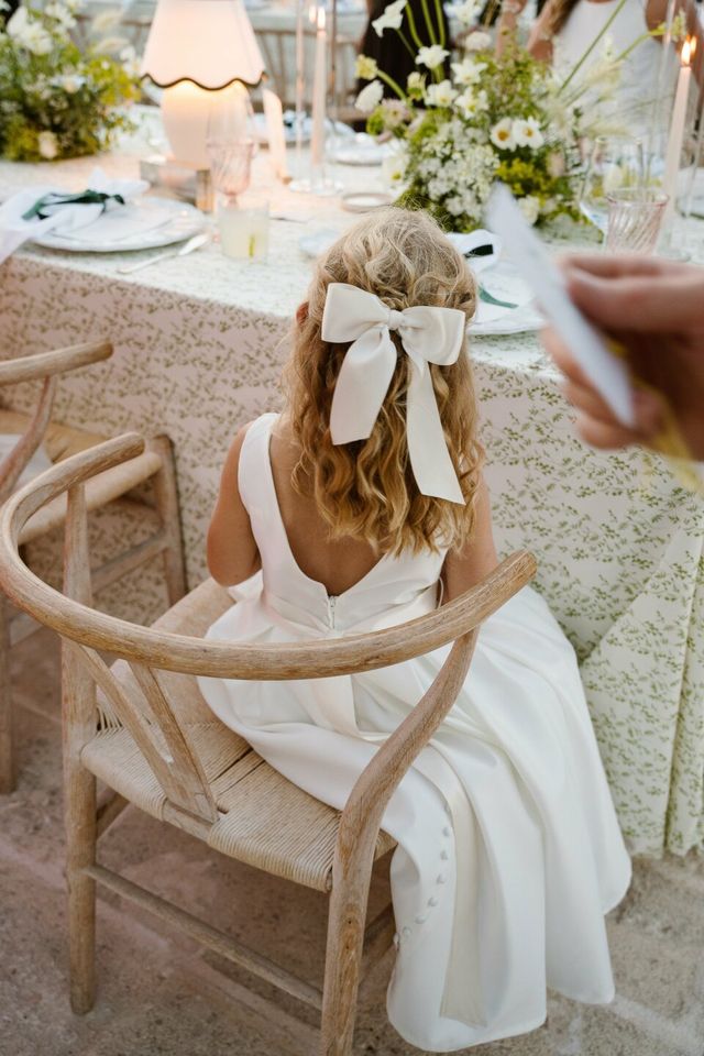 A flower girl with a large white bow in her hair at the wedding.
