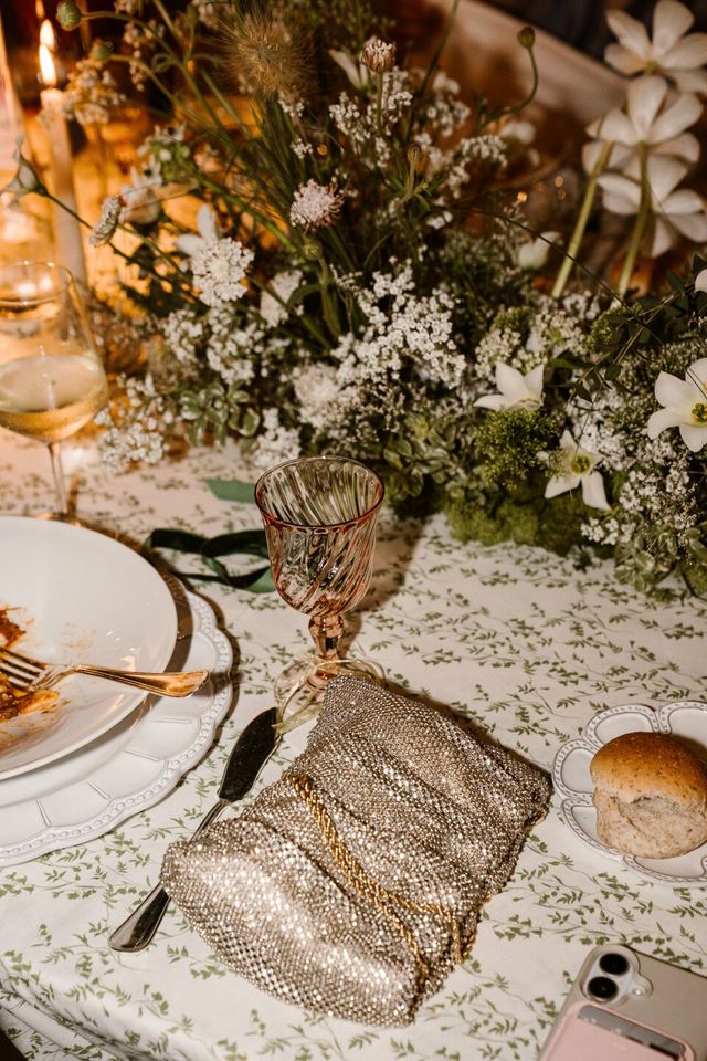 A tablescape detail with a gold-rimmed glass and a metallic gold clutch catching the light.