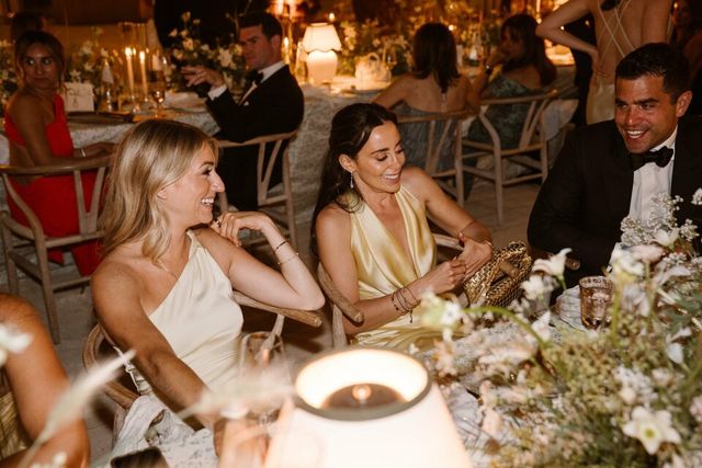 Smiling guests in formal attire sit together at a flower-topped dinner table.