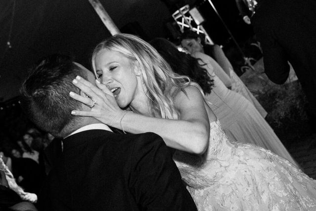 A black and white photo of a laughing bride lifting her partner in celebration.