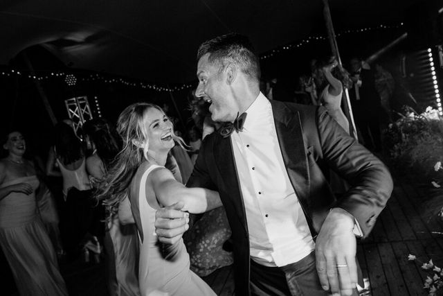 Bruidspaar danst samen en lacht onder een feesttent met lichtjes, sfeervolle openingsdans.