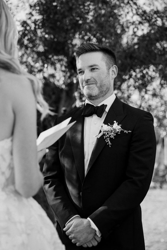 A black and white portrait of a smiling groom in a tuxedo.